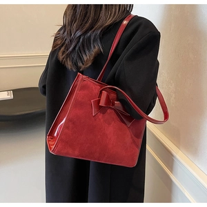 Detailed side view of a large red suede tote bag with decorative bow on a black coat