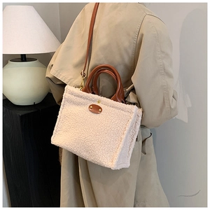 Close-up of beige faux shearling tote with brown leather handles and gold metal details
