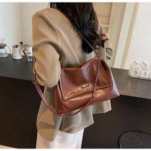 Detail einer braunen Leder-Tote-Tasche mit Kettenriemen und Metallplakette im Café