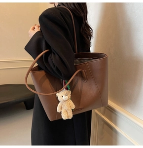 Detail of dark brown leather tote with gold-stamped logo and beige plush bear charm