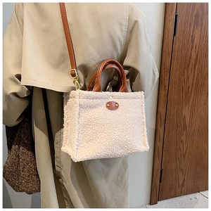 Model wearing a fuzzy beige fleece tote bag with brown handles and a long shoulder strap