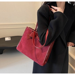 Detail of burgundy faux suede tote bag with elegant bow accent on model's shoulder