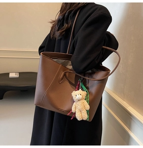 Detail of deep brown pebble leather tote bag with FASHION & BAGS logo and plush bear charm