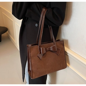 Close-up of brown suede tote bag with shiny leather bow detail and shoulder straps