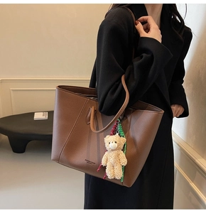 Detail view of brown pebbled leather tote bag featuring a cute plush bear charm accessory