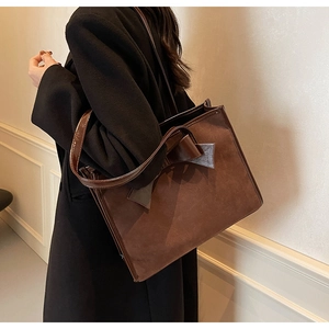 Macro view of dark brown faux suede tote bag showing leather bow detail and texture