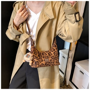 Detail view of leopard print crossbody bag with metal logo and plush lion charm accessory