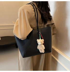 Detail of black pebbled leather tote bag with cute plush bear charm on khaki trench coat