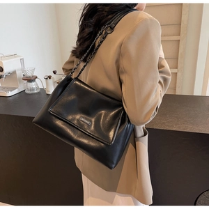 Detail einer schwarzen Lederkette Schultertasche mit Metall-Logo im Café Hintergrund