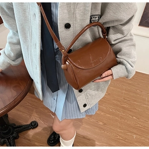 Detailed side view of a glossy vintage brown leather crossbody bag with top handle