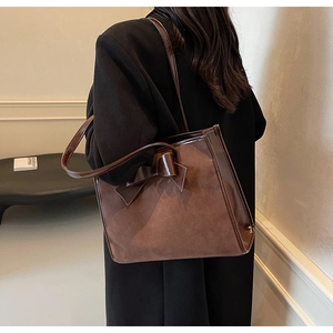 Close-up of brown suede tote bag featuring a large decorative leather bow detail