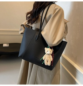 Close-up of black lychee grain tote bag with a plush bear charm and striped ribbon detail