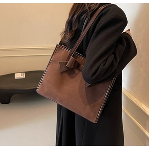 Detail view of large brown suede tote bag with distinctive bow accent on a model's shoulder