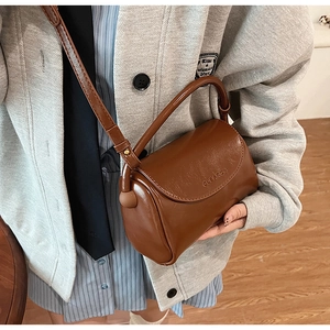 Detail view of brown leather crossbody bag with rounded handle and embossed logo texture