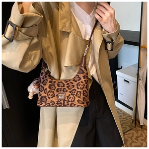 Detailed close-up of leopard print crossbody bag with brown leather strap and plush charm