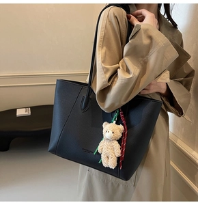 Detail of black pebbled leather tote bag with plush bear charm and striped strap