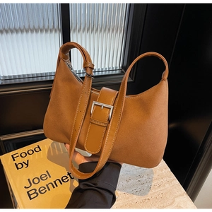 Detail of brown suede underarm bag with metal buckle and glossy trim on marble surface