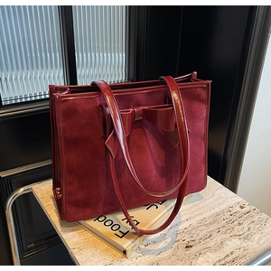 Macro view of burgundy suede tote bag featuring a glossy faux leather bow detail
