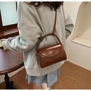 Detail of a brown vintage leather crossbody bag with a curved handle and flap closure