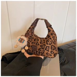 Detail of leopard print handbag featuring leather tag and animal plush charm accessory