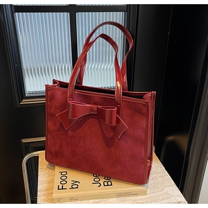 Detail of burgundy faux suede tote bag featuring a large decorative bow and patent leather handles