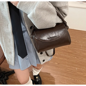 Detail of a dark brown glossy leather handbag featuring an embossed logo on the flap cover