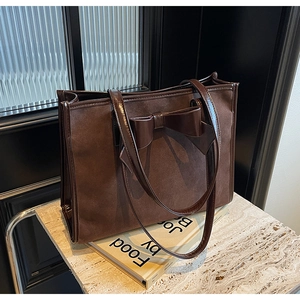 Close-up of chocolate brown tote bag showing the suede texture and patent leather bow detail