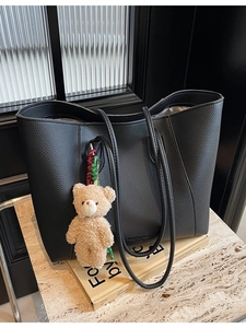 Black pebble leather large tote bag with cute plush bear charm on minimalist background