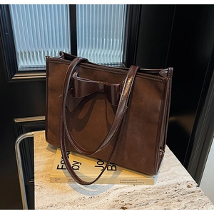 Detail of dark brown suede tote bag with glossy faux leather bow and textured finish