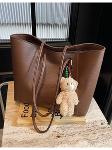Brown faux leather tote bag with teddy bear pendant on books in a minimalist setting