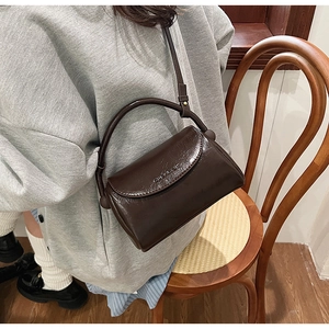 Detail of a shiny dark brown leather satchel with top handle and adjustable shoulder strap