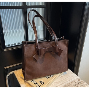 Detail of dark brown faux suede tote bag featuring a large decorative bow and leather trim