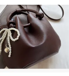 Detail der dunkelbraunen Leder-Eimertasche mit geknotetem Griff und Perlenanhänger