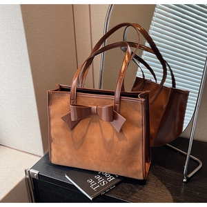 Detailed close-up of brown suede tote bag with leather bow decoration on a wooden surface