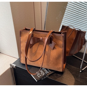 Close-up of brown suede tote bag with large bow detail and faux leather trim textures