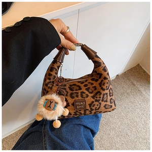 Detail of leopard print crossbody bag featuring a leather brand tag and plush lion charm