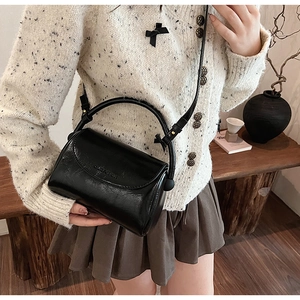 Detailed side view of glossy black PU leather handbag with decorative bow on the handle