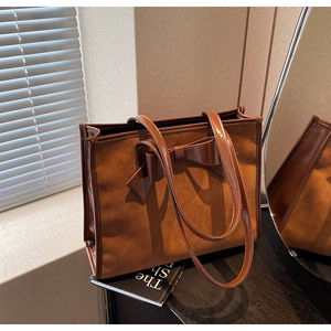 Close-up of vintage brown tote bag featuring a decorative bow and textured suede finish