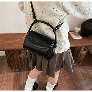 Detail of minimalist black leather square bag worn with crossbody strap in a cozy home setting