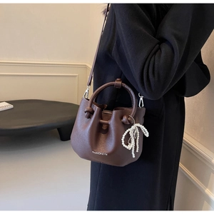 Detail der braunen Falten-Eimertasche mit Rundgriff und weißem Perlenbogen-Anhänger