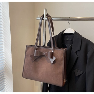 Close-up of a large coffee brown suede tote bag featuring a decorative leather bow design