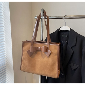 Detail of a brown faux suede tote bag featuring a leather bow and smooth shoulder straps