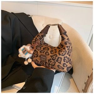 Detail of leopard print handbag with leather logo tag and plush lamb charm on a sofa