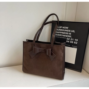 Detail view of deep brown suede tote bag featuring a large decorative leather bow accent