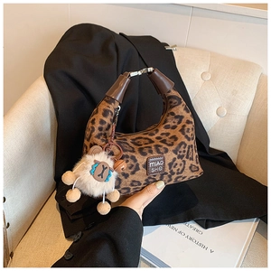 Detail of leopard print handbag with plush doll charm on a stylish fabric chair