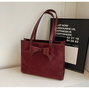 Detail of burgundy suede tote bag featuring a glossy patent leather bow and thin straps