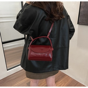 Detail of burgundy glossy patent leather handbag with adjustable strap on a leather jacket
