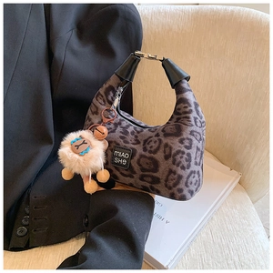Detail of leopard print crescent bag featuring metal zipper and alpaca charm on chair