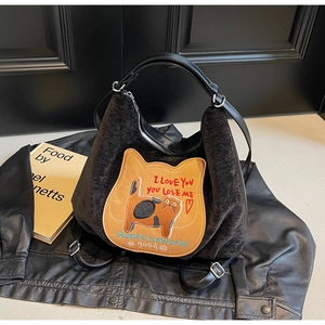 Close-up of black corduroy hobo bag featuring a cat patch and embroidery on a leather jacket