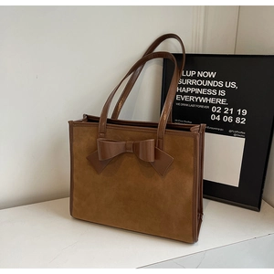 Detail view of caramel suede tote bag with large decorative bow on white marble